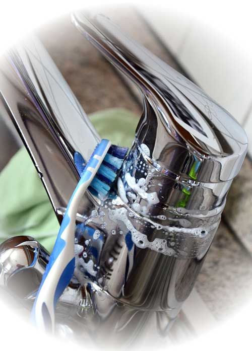 Wasserhahn, der gerade mit der Zahnbürste gereinigt wird